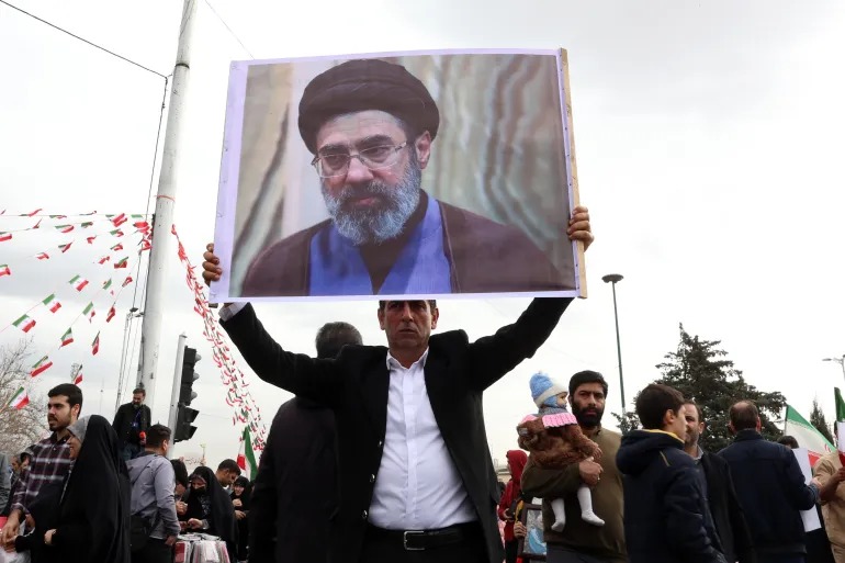 Seorang pria Iran memegang foto Mojtaba Khamenei, putra pemimpin tertinggi Iran saat itu, ketika ia ikut serta dalam perayaan ulang tahun ke-47 revolusi Islam di Teheran, Iran, 11 Februari 2026. (Sumber Foto: Abedin Taherkenareh/EPA via Al Jazeera)